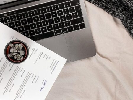 A laptop keyboard with a small potted succulent and a résumé on a white fabric surface, depicting a modern setup to write a resume.