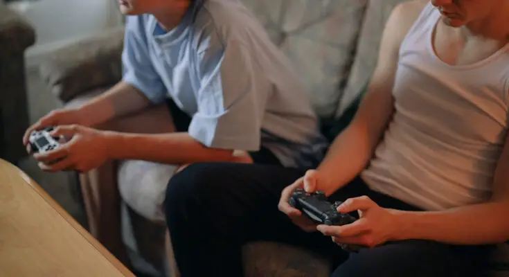 Two young people sitting on a couch, each holding a video game controller, focused intently on playing one of the best sports video games.