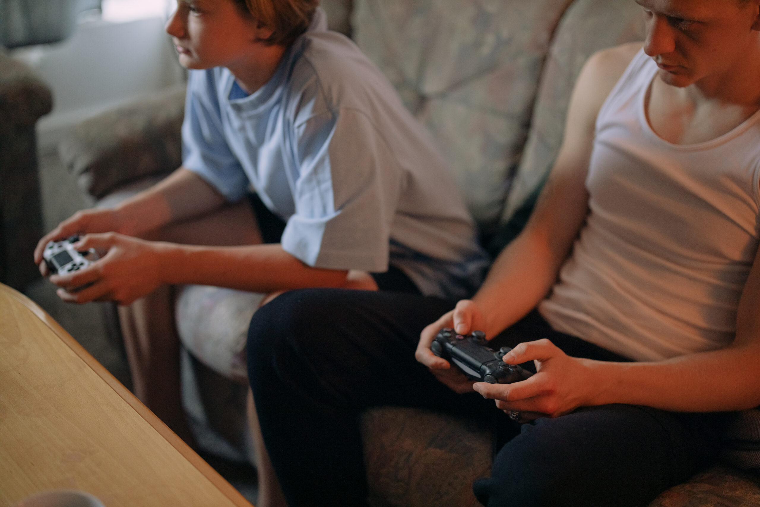 Two young people sitting on a couch, each holding a video game controller, focused intently on playing one of the best sports video games.