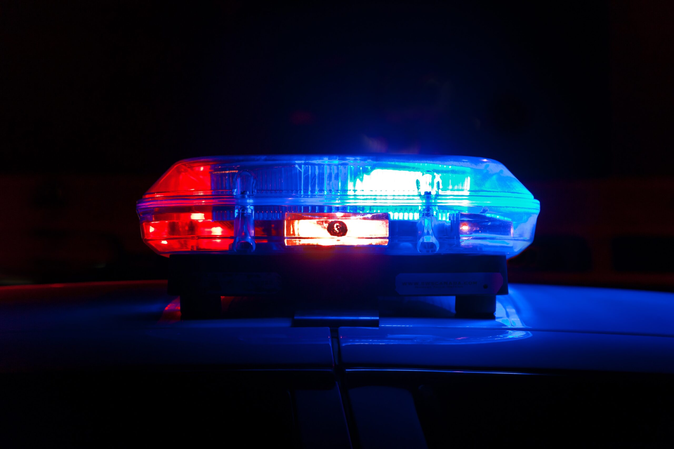 A close-up of police cars' illuminated red and blue siren lights against a dark nighttime background.