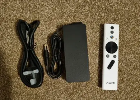 HDMI cable, power adapter, and a remote control for XGIMI Halo+ brand electronics neatly arranged on a carpeted floor.