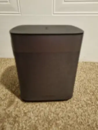 A slightly blurry image of a dark-colored XGIMI portable projector positioned on a carpeted floor against a white wall.