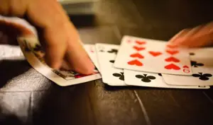 Hands dealing playing cards on a wooden table, focusing on cards in motion with a blur effect to suggest movement, embody myths about bad poker hands. Visible cards include a queen of spades and a series