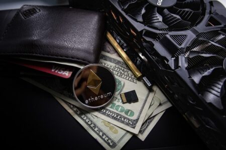 A close-up image featuring a black wallet with cash and cards, a Visa card visible, an Ethereum coin showcasing cryptocurrency, and part of a graphics card.