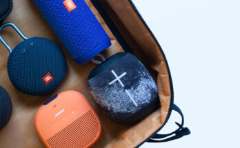 A collection of various Bluetooth speakers in different shapes and colors neatly arranged in a brown bag against a white background.