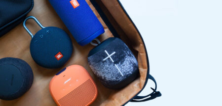 A collection of various Bluetooth speakers in different shapes and colors neatly arranged in a brown bag against a white background.