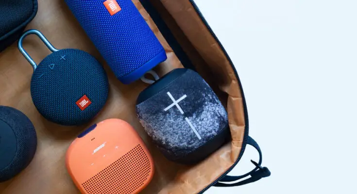 A collection of various Bluetooth speakers in different shapes and colors neatly arranged in a brown bag against a white background.