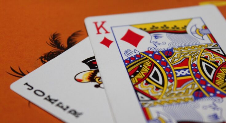 A close-up photo of playing cards on an orange surface, focusing on the king of diamonds card partially overlaid by another card in a betting system setup.