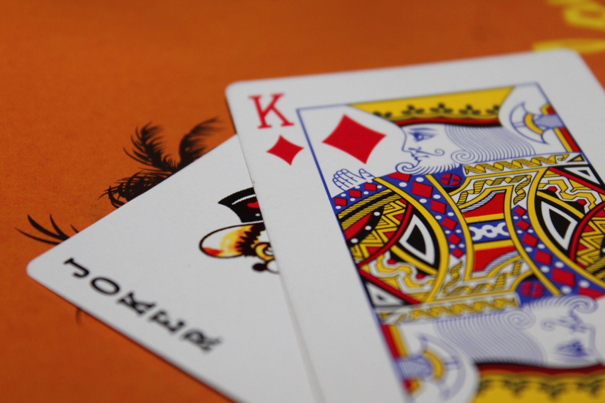 A close-up photo of playing cards on an orange surface, focusing on the king of diamonds card partially overlaid by another card in a betting system setup.