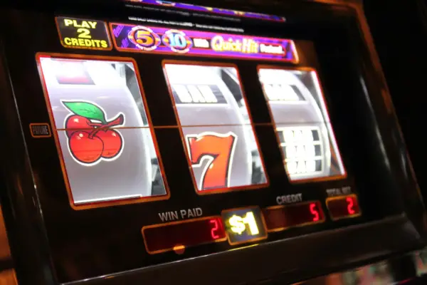A vibrant Call Slots machine displaying cherry and lucky seven symbols on its reels, highlighting the play credits and winnings on a dimly lit casino floor.